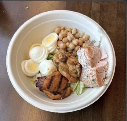 A plate of grilled chicken, salmon, eggs and chickpeas over salad